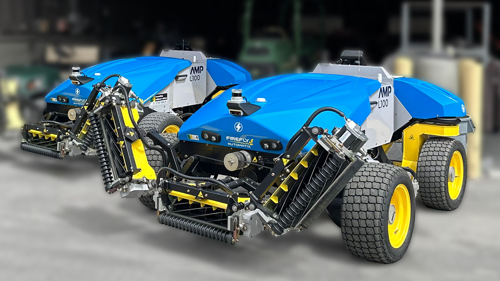 Two FireFly AMP mowers in front of a shop