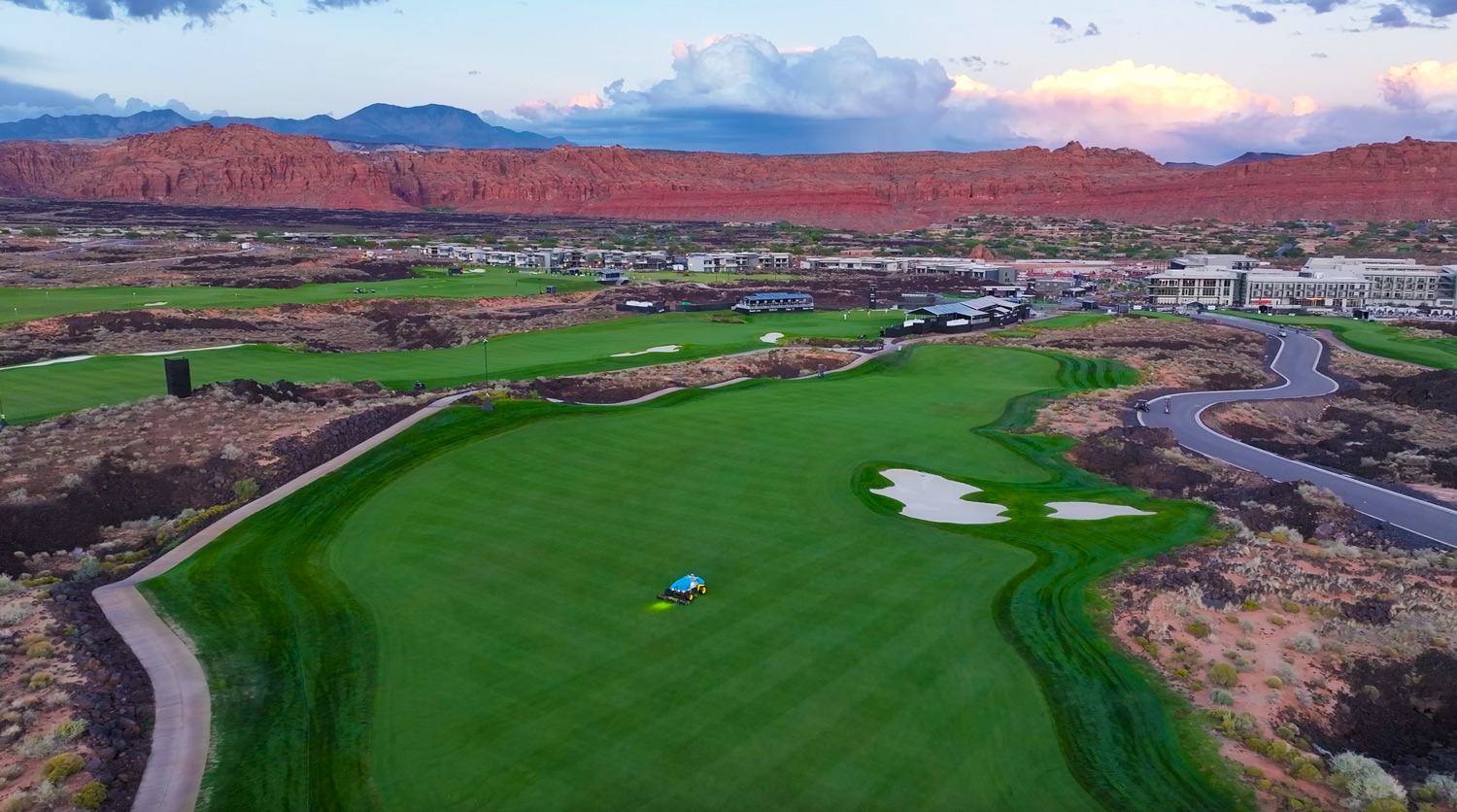 FireFly robotic fairway mower with green grass mown in checkerboard pattern and red rock cliffs in background